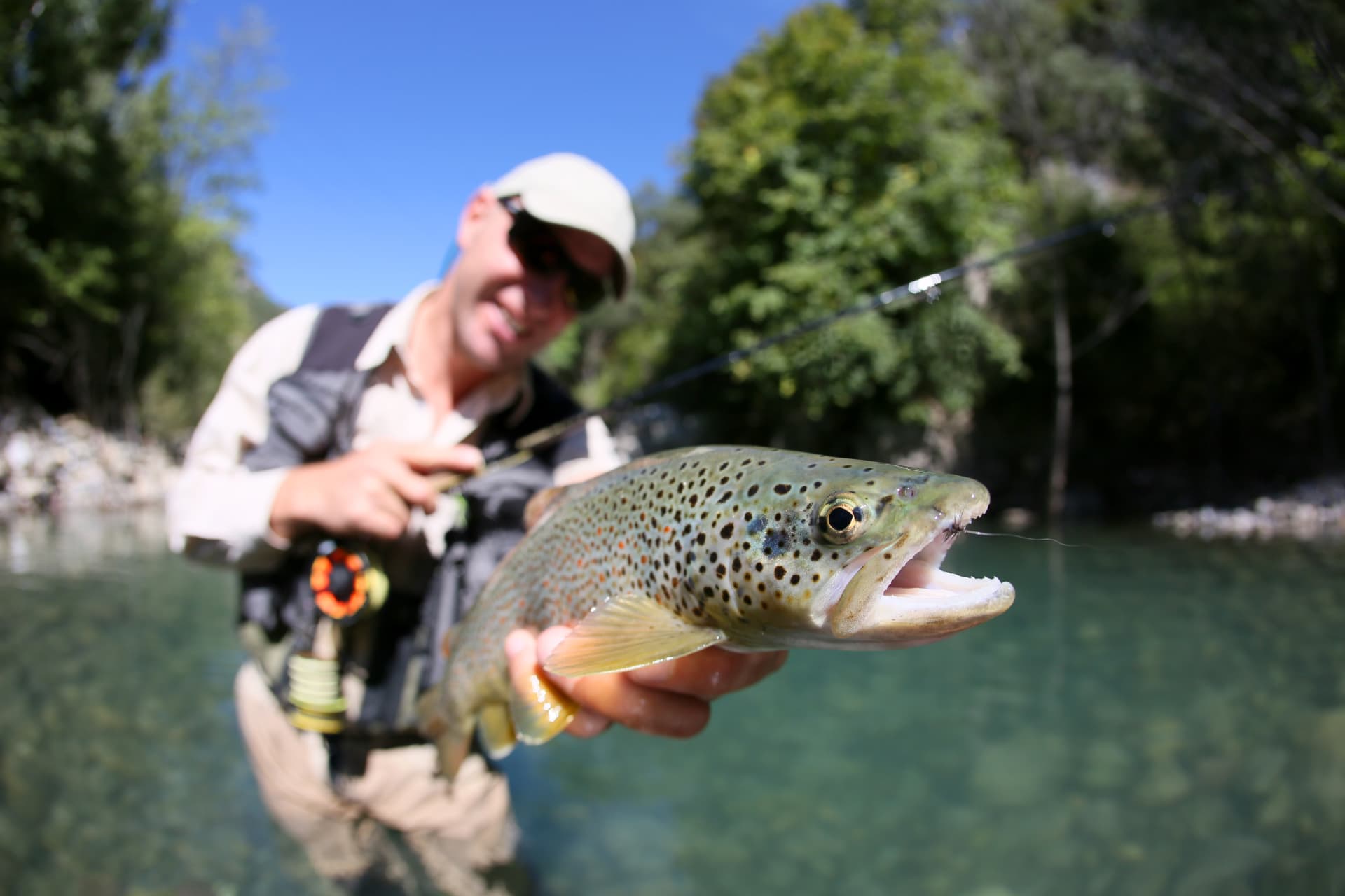 Fischer mit einer Forelle im Vordergrund am Fluss