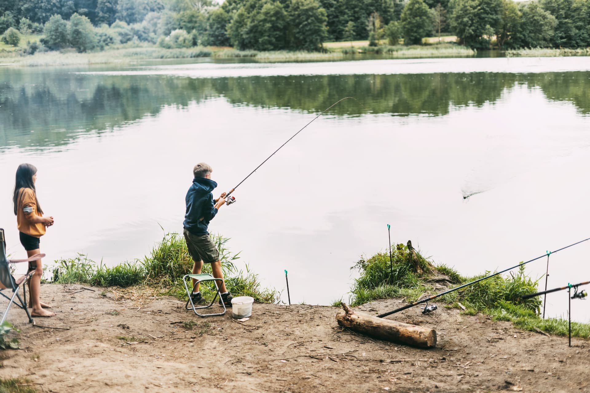 Zwei Kinder beim Fischen am See, der Junge hält eine gebogene Angelrute